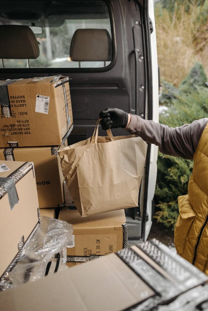 pexels-photo-6407565 A courier handling packages and paper bags in a van for delivery service.